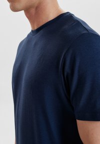 Mørkeblå bomulds-t-shirt med rund halsudskæring og korte ærmer. Glat overflade, minimale sømme, tætsiddende ved skuldrene.