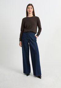 Pull en brun foncé avec un col rond, assorti à un jean en denim noir à taille haute et jambes larges. Texture lisse et design minimaliste.