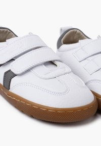 Scarpe sintetiche bianche per bambini con due strap in velcro, dettagli grigi, punte arrotondate e una suola in gomma marrone texturizzata.