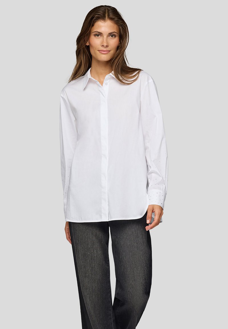 White button-up shirt features long sleeves with dotted accents, a classic collar, and a relaxed fit, paired with dark wide-leg pants.