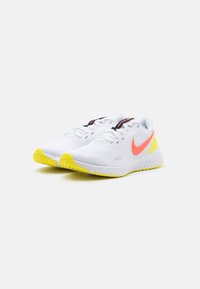 Bílé běžecké boty s texturovaným síťovaným svrškem, s růžovým a žlutým logem Swoosh a žlutou gumovou podrážkou.