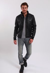 Schwarze Leder-Bomberjacke mit Vordertaschen, graues Rundhals-T-Shirt, hellblaue verwaschene Jeans und schwarze Stiefeletten.