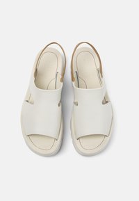 White leather sandals with a smooth finish, open heel, and cut-out design. Features a tan strap and visible stitching detail.