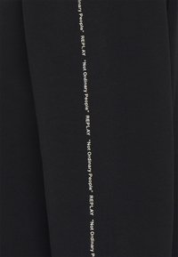 Joggers neri in tessuto con una vestibilità slim, caratterizzati da un branding testuale bianco lungo i lati che recita "REPLAY" e "Not Ordinary People."