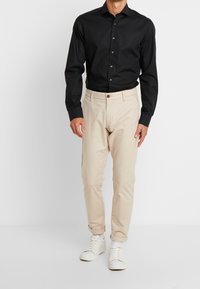 Svart långärmad skjorta med knappar, i kombination med ljusbeige chinos och vita sneakers. Outfitten har en figursydd silhuett.