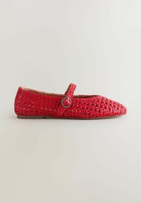 Piros szőtt Mary Jane lapos cipő hegyes orral és ezüst csatos pánttal, bézs háttéren.