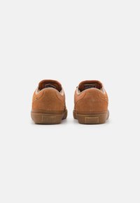 Zapatillas de ante marrón con suelas de goma, que presentan un diseño de caña baja y acentos en tono marrón claro. Los talones tienen una marca grabada.
