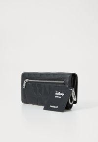 Portefeuille en cuir noir avec des motifs en relief, une fermeture éclair en argent et un fermoir. Comprend une étiquette avec les marques "Disney" et "Desigual".