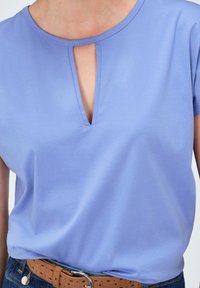 Lila korte mouwen top met een uitsparing in de hals, gemaakt van zachte stof. Gecombineerd met een bruine geperforeerde riem en denim jeans.