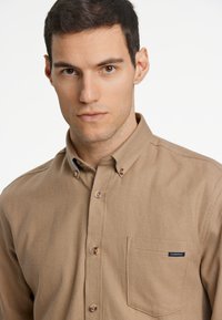 Lichtbruin shirt met een visgraatpatroon, voorzien van een button-down kraag, een borstzak en bruine knopen. Logo-tag op de zak.