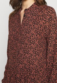 Blůza s červeným a černým vzorem, s stojáčkovým límcem, knoflíkovou léga a dlouhými rukávy. Tkanina se zdá být jemná s texturovaným, lehkým pocitem.