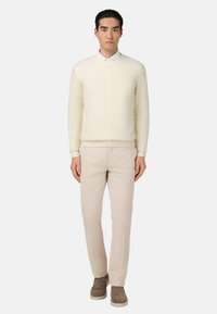 Suéter de punto color crema con escote redondo, combinado con pantalones beige claros y botas de tobillo gris marrón. Diseño simple, corte relajado.