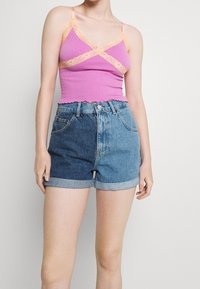 Dopasowany różowy top na ramiączkach z prążkowanej tkaniny, wykończony koronką i falbaniastym dołem, połączony z szortami dżinsowymi o wysokim stanie z wywiniętym dołem w różnych odcieniach niebieskiego.