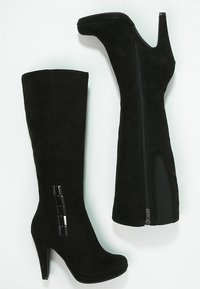Bottes noires en daim montantes avec un bout pointu, un talon haut et une fermeture éclair sur le côté. Présente des accents verticaux brillants sur le côté extérieur.