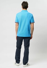 Blå polo shirt med en ensartet tekstur, der har kontrasterende stribede mansjetter. Kombineret med mørkeblå bukser og hvide sneakers.