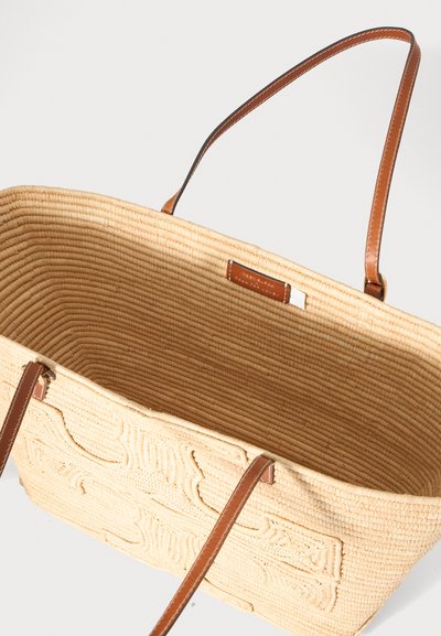 Sac cabas en paille tressée avec des bandoulières en cuir marron et motif floral embossé sur le panneau avant, présenté vide et ouvert.