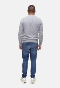 Maglione grigio a maniche lunghe realizzato in tessuto a maglia, abbinato a jeans in denim blu con due tasche posteriori e cuciture chiare. Sneakers bianche completano il look.