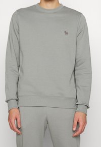 Sudadera gris claro hecha de una mezcla de algodón; presenta mangas largas, puños de canalé y un pequeño logo estampado en el pecho.