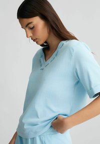 Top azzurro chiaro a maniche corte con scollo a V e dettagli ricamati lungo il collo, caratterizzato da una vestibilità comoda e una texture morbida.