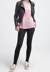Schwarze, figurbetonte Leggings, ein hellrosa Satin-Top und eine schwarze Lederjacke mit gerippten Akzenten. Abgerundet mit roségoldenen Sneakern.