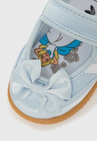 Světle modrá dětská bota s atlasovou mašlí a stélkou s obrázkem kreslené dívky v modrobílých šatech obklopené květinami.