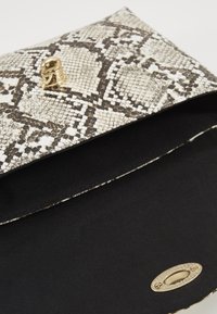 Clutch con stampa serpente in beige e nero, con esterno testurizzato, chiusura in hardware dorato e interno in stoffa nera solida.