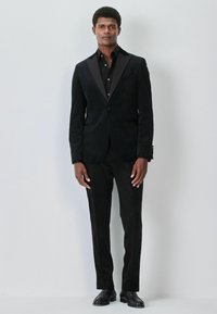 Black velvet blazer with satin lapels, paired with a black dress shirt and textured black trousers. Finished with black leather shoes.