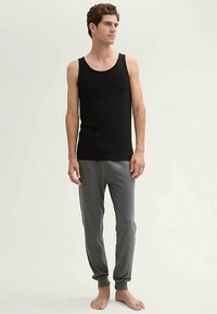 Črna bombažna majica brez rokavov, kombinirana z sivimi trenirkami z manšetami. Obleka je preprosta, z neformalnim krojem in mehko teksturo.