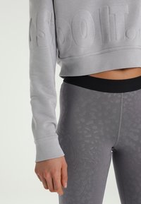 Grijze, cropped sweatshirt met reliëflettering en lange mouwen, gecombineerd met hooggesneden grijze legging met een subtiel patroon.
