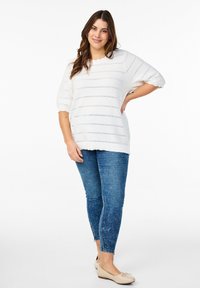 Lös passform vit stickad tröja med horisontell struktur, matchad med blå smala jeans och beige ballerina-skor. En enkel och avslappnad outfit.