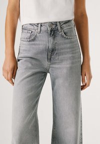 Vaqueros de pierna ancha de color gris claro hechos de mezclilla, con cintura alta, bolsillos delanteros y un desgaste sutil para un aspecto texturizado.