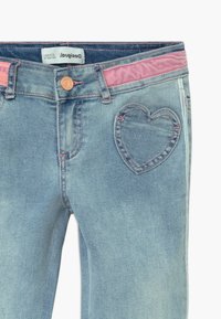 Světle modré deniminové džíny s růžovým pasem, srdíčkovým prošíváním na zadní kapse a kontrastním prošíváním podél švů.