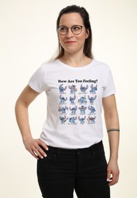 Bílý bavlněný tričko s různými výrazy animovaných postaviček a popisky. Design zdůrazňuje emoce, potištěné v živých barvách.