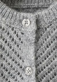 Närbild av en ljusgrå stickad kofta med två runda vita knappar och en ribbad krage.