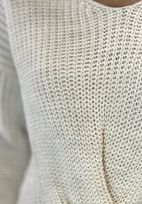 Helles beige gestricktes Sweatshirt mit einem strukturierten Muster, das lockere Maschen und einen lässigen Schnitt aufweist. Sichtbare Nähte sorgen für einen entspannten Fall.