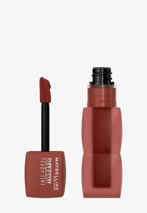 Maybelline Superstay Teddy Tint, mit einer matten Terrakotta-Farbe, weichem Applikator und einem rechteckigen Glasbehälter mit schwarzem Deckel.