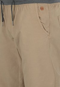 Shorts beiges en tissu léger, dotés d'une taille élastique avec cordon de serrage et de poches latérales. Détails subtils avec un accent logo rond.