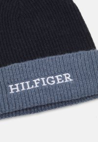 Beanie a coste in blu navy e azzurro chiaro con risvolto; presenta il logo bianco "HILFIGER" sul risvolto. Texture morbida e design classico.