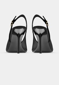 Black high-heeled slingback shoes with thin stiletto heels and gold buckle straps shown from the back on a white background.