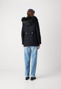 Laivyno spalvos paltas su dirbtinio kailio gaubtu, vieno mygtuko dizainas ir nugaros detalėmis su dviem mygtukais ir klostėmis. Nešiojamas su šviesiai mėlynomis džinsomis.