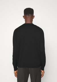 Czarny dzianinowy sweter z długimi rękawami, okrągłym dekoltem i gładką fakturą. Projekt charakteryzuje się dopasowanym krojem i prążkowanymi mankietami.