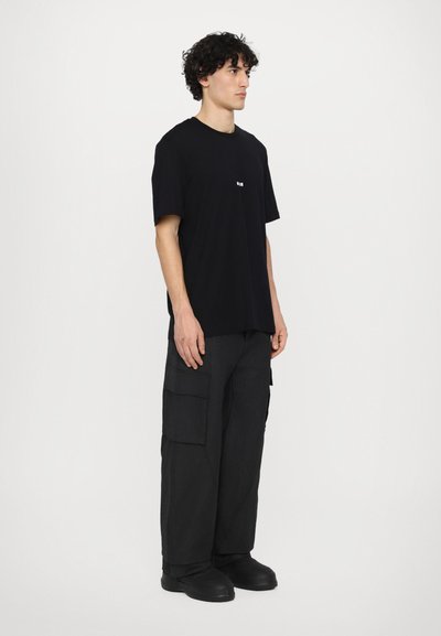 Black cotton t-shirt with short sleeves and a small front graphic, paired with loose-fitting black cargo pants featuring side pockets.