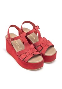 Red suede wedge sandals featuring a T-strap design with woven detailing. The platform is solid and complements the textured upper.