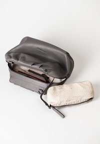 Gray leather bag with a textured finish, zip closure, and gathered top; includes a small cream pouch with a geometric pattern and zipper.