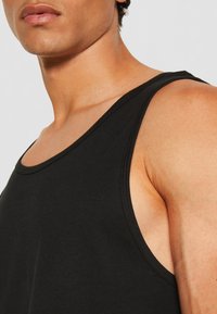 Black cotton tank top with wide armholes and a rounded neckline. Features a smooth texture and minimal stitching details.