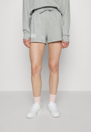 Bermudas cinzas de algodão com uma cintura elástica e cordão, apresentando um emblema branco. Combinadas com ténis brancos e meias rosas.