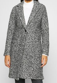 Grå och vit strukturerad ullrock med slagkrage, enkel knappstängning och sidofickor. Långa ärmar med manschettdetaljer.