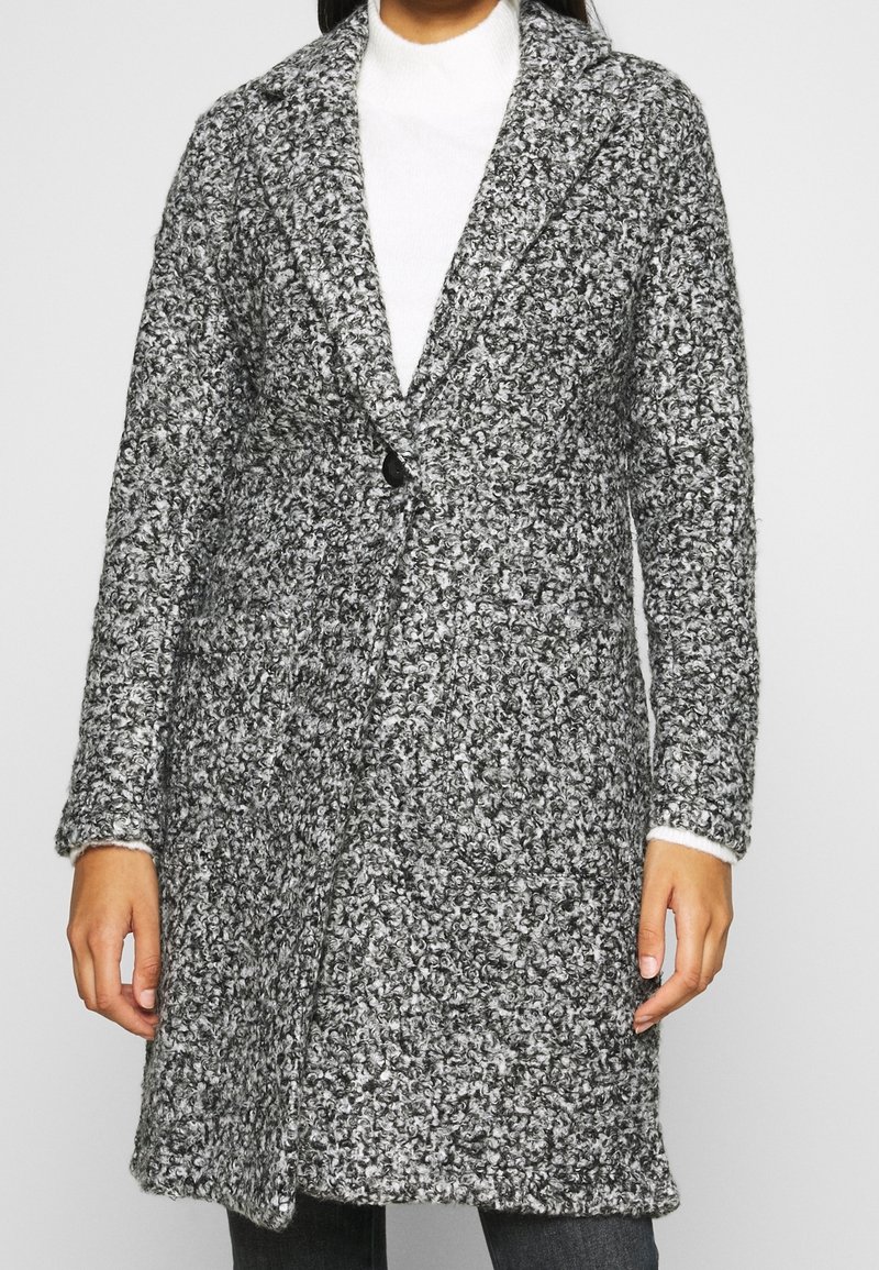 Grå och vit strukturerad ullrock med slagkrage, enkel knappstängning och sidofickor. Långa ärmar med manschettdetaljer.