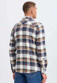 Gecontroleerd flanellen shirt in blauw, geel en wit. Heeft lange mouwen en knoopmanchetten, met een klassieke kraag en een afgeronde zoom.