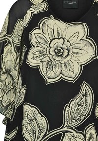 Blusa negra con estampado floral que presenta grandes flores y hojas en color crema, escote en V y una tela suave y ligera con un diseño translúcido.